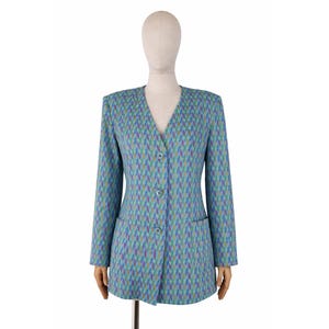 Puede incluir: Un blazer estampado en tonos azules, morados y verdes, exhibido en un maniquí. El blazer presenta un cuello en V, mangas largas, dos bolsillos delanteros y tres botones. La tela tiene un diseño geométrico.