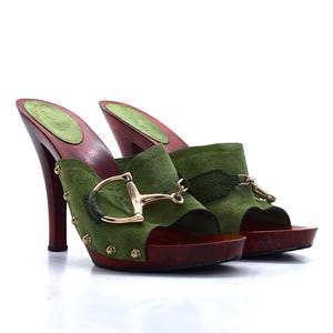 May include: A pair of green suede clogs with wooden soles and heels. The clogs feature gold-colored hardware and studs. The heels are dark red, and the footbed is green. The clogs are a stylish footwear option.