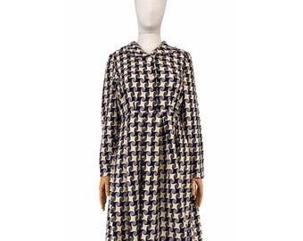 May include: A knee-length dress featuring a repeating geometric pattern of dark navy blue and cream-coloured swirling shapes. The garment has long sleeves, a pointed collar, and a button-down front closure with a fitted waist and a pleated skirt.