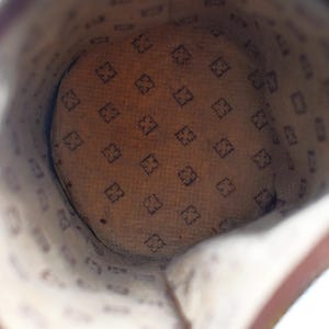 Puede incluir: Vista interior de un bolso de cuero marr&oacute;n. El forro interior presenta un patr&oacute;n repetido de una letra "F" estilizada en forma de diamante. El interior del bolso es de color beige claro y el exterior de cuero es marr&oacute;n oscuro.