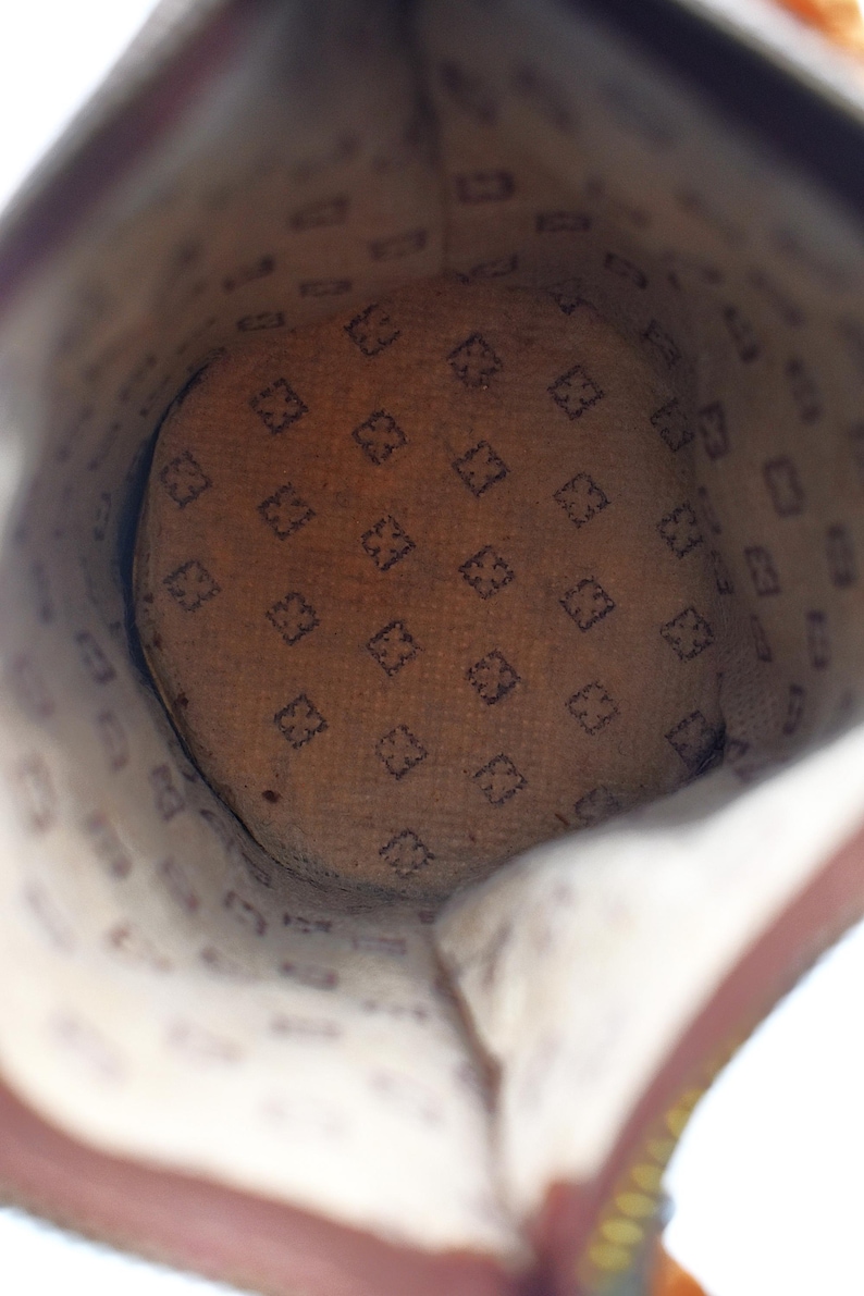 Puede incluir: Vista interior de un bolso de cuero marr&oacute;n. El forro interior presenta un patr&oacute;n repetido de una letra "F" estilizada en forma de diamante. El interior del bolso es de color beige claro y el exterior de cuero es marr&oacute;n oscuro.