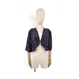 Può includere: Una giacca corta nera con stampa floreale colorata. La giacca ha un collo a V e maniche corte.