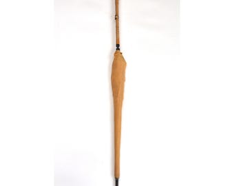 Puede incluir: Un paraguas vintage con un mango de madera curvado y una capota de tela beige. El mango está envuelto en un material texturizado y el paraguas tiene una punta negra. El paraguas está de pie sobre un fondo blanco.