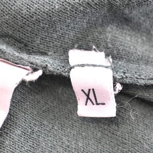 May include: Close-up of a dark green fabric with a pink tag. The tag is white with the letters "XL" printed in black. The fabric appears to be a knit or woven material.