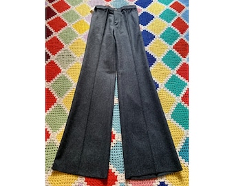 May include: Dark gray wide-leg pants with a high waist. The pants are made of a textured fabric and have a classic design. The pants are displayed on a colorful, patterned blanket.