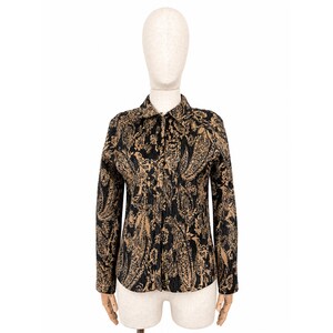 May include: A long-sleeved button-down shirt with a black and gold paisley pattern. The shirt has a classic collar and is displayed on a mannequin. The fabric appears to have a textured, ribbed effect.