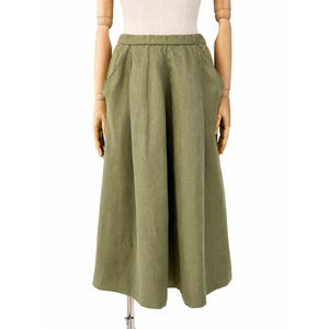 Peut inclure: Une jupe mi-longue vert olive dotée d'une taille haute élastiquée, de poches latérales et d'une coupe évasée à jambes larges qui tombe sous les genoux. Le vêtement est confectionné dans un tissu texturé avec un tissage visible.