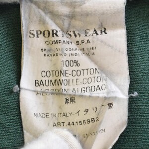 May include: Close-up of a white tag with black text, attached to a green fabric. The tag reads "SPORTSWEAR COMPANY S.P.A." and includes details about the fabric composition, including "100% COTONE-COTTON". The tag also states "MADE IN ITALY."