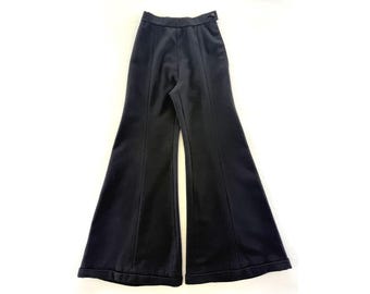 May include: Black flared pants with a high waist and a button closure. The pants have vertical seams down the front and are made of a solid, dark fabric. The wide leg design creates a retro silhouette.