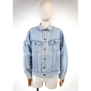 Può includere: Una giacca in denim azzurro con colletto classico, maniche lunghe e chiusura frontale con bottoni. Il capo presenta due tasche sul petto con patta abbottonata e dettagli con cuciture verticali sui pannelli anteriori.