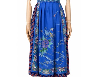 May include: A blue skirt with a floral and bird design. The skirt has a wide waistband with a detailed pattern and a full, pleated silhouette. The main design includes a large rose and a bird, with additional floral and landscape elements.