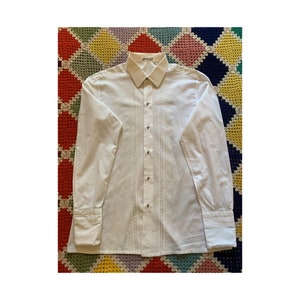 Puede incluir: Una camisa blanca de manga larga con botones, diseño texturizado y cuello puntiagudo.