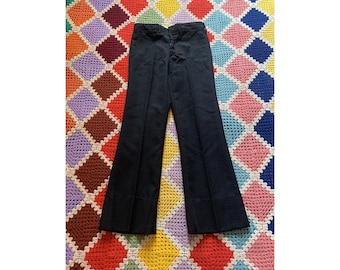 May include: A pair of black flared pants with a straight leg and a wide leg opening. The pants are made of a textured fabric and have a zipper fly and button closure.