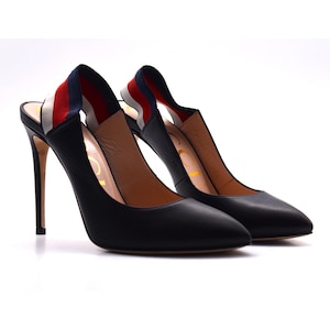 Peut inclure: Une paire d'escarpins noirs à talons hauts et bouts pointus. Les talons sont fins et hauts. Les brides arrières sont rayées de rouge, blanc et bleu. Les chaussures sont sur fond blanc.
