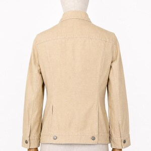 May include: A beige jacket with a button-down front, long sleeves, and two small pockets. The jacket has a classic design with a collar and buttoned cuffs. The jacket is displayed on a mannequin.