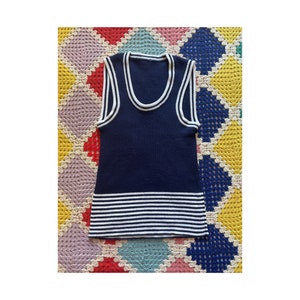 Può includere: Un top di maglia blu navy senza maniche con bordino bianco intorno al collo e una fascia a righe bianche e blu in fondo.