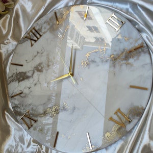 Peut inclure: Un cadran d'horloge rond en marbre blanc avec des chiffres romains dorés et des aiguilles dorées. Le cadran de l'horloge a un effet de marbrure dorée subtil.