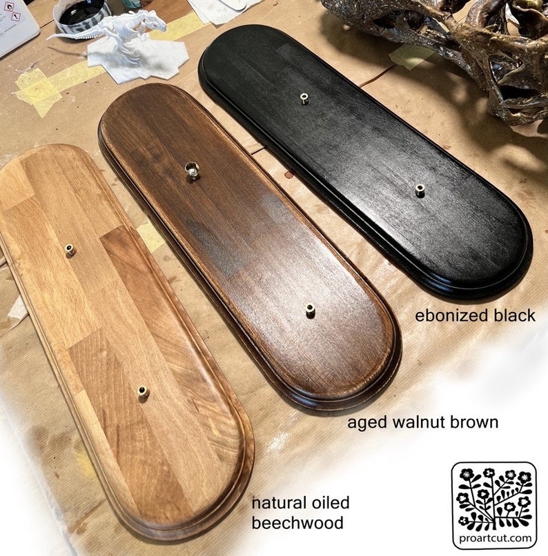 Op de afbeelding: Drie houten displayplaten in natuurlijk geolied beukenhout, verouderd walnootbruin en ebbenzwart. Elke plaat heeft een messingkleurig montagegat. De platen zijn ovaal van vorm met afgeronde randen.