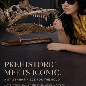 Op de afbeelding: Een fossiel-ge&iuml;nspireerde dinosaurus schedel replica op een houten voet, met de tekst "PREHISTORIC MEETS ICONIC." De afbeelding toont ook een persoon met een zonnebril die lippenstift aanbrengt. Een statement stuk voor de durfals.