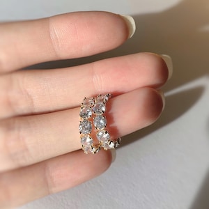 Peut inclure: Deux bagues en or avec des pierres rondes transparentes serties en pavé. Les bagues sont empilées l'une sur l'autre.