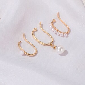 Puede incluir: Conjunto de tres pendientes de aro dorados con detalles de perlas. Dos pendientes tienen una sola perla, mientras que el tercer pendiente tiene una fila de perlas.