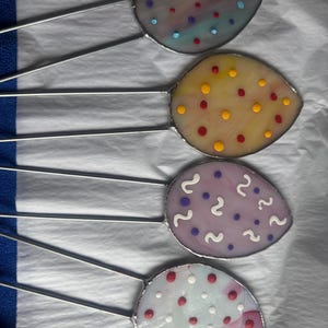 May include: Four glass ornaments with different patterns. The ornaments are on metal sticks. The patterns include polka dots, swirls, and zigzags. The colors are red, blue, yellow, purple, and white.