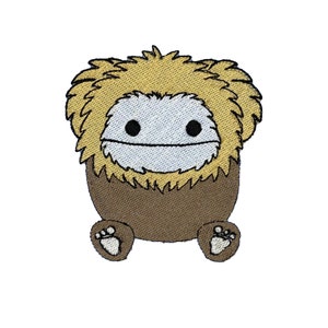 Pode incluir: Um remendo bordado com uma criatura de desenho animado com uma cabeça peluda e um rosto sorridente. A criatura é marrom e amarela e tem pequenos pés marrons.