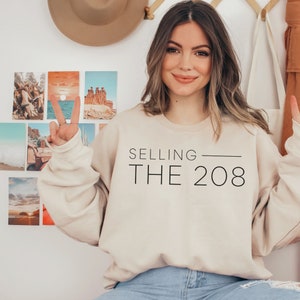 May include: A beige sweatshirt with the text "SELLING THE 208" printed in black.