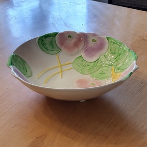 May include: A white ceramic bowl with a floral design. The bowl has green leaves and pink flowers. The bowl is on a wooden table.