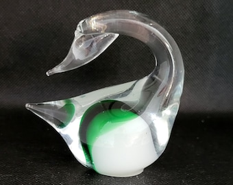 May include: A clear glass swan figurine with a green and white swirl design. The swan's neck is curved and its head is tilted down.