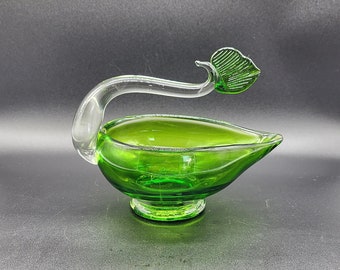 May include: A green glass swan-shaped dish with a clear glass neck and a green leaf on top.