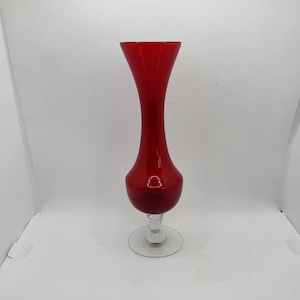 May include: A red glass vase with a clear glass base. The vase has a narrow neck and a wide, rounded body.