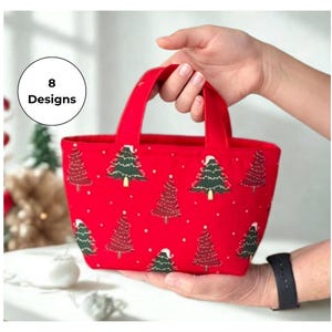 May include: A small red fabric tote bag featuring a repeating pattern of green and red Christmas trees with white snow accents. The bag has two short handles and a circular graphic in the upper left corner with the text 8 Designs.