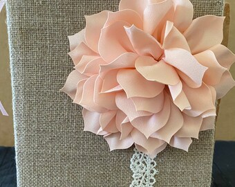 May include: A burlap covered box with a large pink fabric flower and white lace trim. The box is a great way to store small items or to use as a decorative piece.