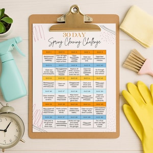 May include: A clipboard with a 30-day spring cleaning challenge checklist, a light blue spray bottle, a small potted plant, a silver alarm clock, a yellow rubber glove, a pink brush, and a yellow cleaning cloth. The checklist includes cleaning tasks for each day.