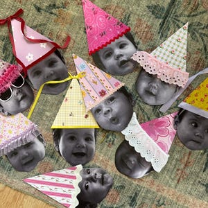 May include: A collection of party hats with baby faces, in black and white, with various patterns and colors. The hats are pink, yellow, and green, with ribbons and lace. The theme is a baby's birthday party.