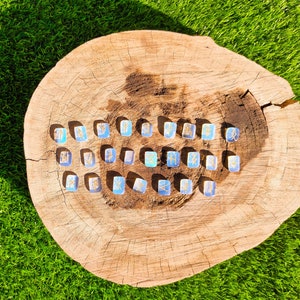 May include: A collection of 25 blue and silver rune stones with gold lettering on a wooden surface. The runes are arranged in a circle.