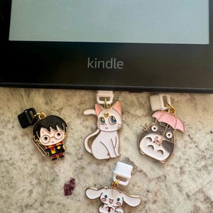 May include: Four colorful book markers with different characters. A black and red Harry Potter character, a white cat with a crescent moon, a gray Totoro character holding a pink umbrella, and a white puppy with pink ears.