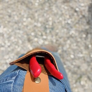May include: A brown leather tool belt with a pocket that holds a pair of red pruning shears.