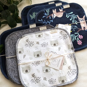 May include: A set of 10 reusable cloths with a white background and a pattern of brown bears and black dots. The cloths are folded and tied with twine and a small tag that reads "SOYA & KOALA, FAIT AU QUÉBEC".