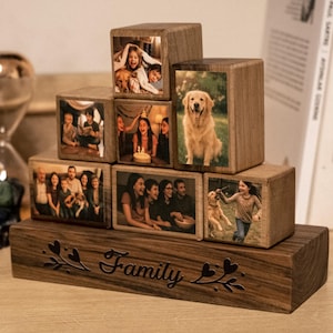 Può includere: Un set di blocchi foto in legno a tema familiare. I blocchi sono impilati a forma di piramide e presentano foto di una famiglia, incluso un cane. La base del set è un blocco di legno con la parola "Famiglia" incisa su di esso.