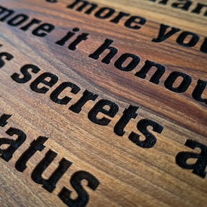 May include: Close-up of a wooden cutting board with the text "The more it honours its secrets are status" engraved in black.