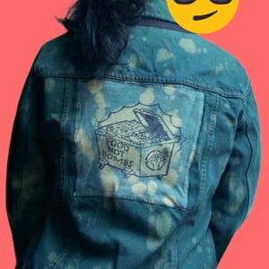May include: Dark teal denim jacket with a bleached pattern. A patch on the back features a drawing of a dumpster overflowing with food, with the words "FOOD NOT BOMBS" and a fist symbol.