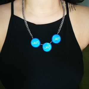 May include: A silver chain necklace with three blue bottle caps that say "LAUT" on them.