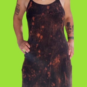 May include: A black sleeveless dress featuring a bleach-dyed pattern with irregular orange and rust-coloured spots throughout the fabric. The garment has thin spaghetti straps, a scoop neckline, and a straight-cut silhouette that falls above the knee.