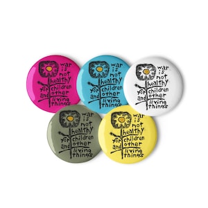 Puede incluir: Un conjunto de cinco botones redondos en varios colores: rosa, azul, blanco, verde oliva y amarillo. Cada botón presenta un diseño gráfico similar a un sol y el texto "war is not healthy for children and other living things."