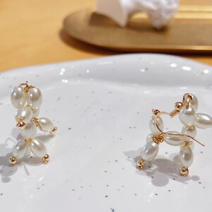 May include: A pair of pearl and gold earrings shaped like a poodle. The earrings are on a white surface.