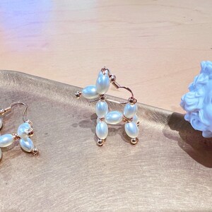 May include: A pair of gold hoop earrings with white pearl beads. One earring is shaped like a flower and the other is shaped like a dog.