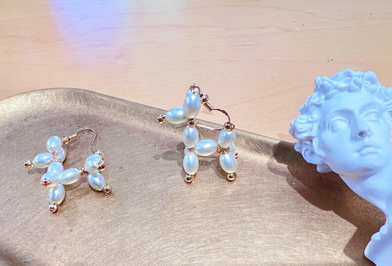 May include: A pair of gold hoop earrings with white pearl beads. One earring is shaped like a flower and the other is shaped like a dog.
