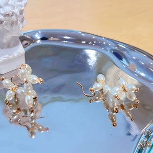 May include: A pair of gold earrings shaped like balloon dogs, made with white pearl beads.